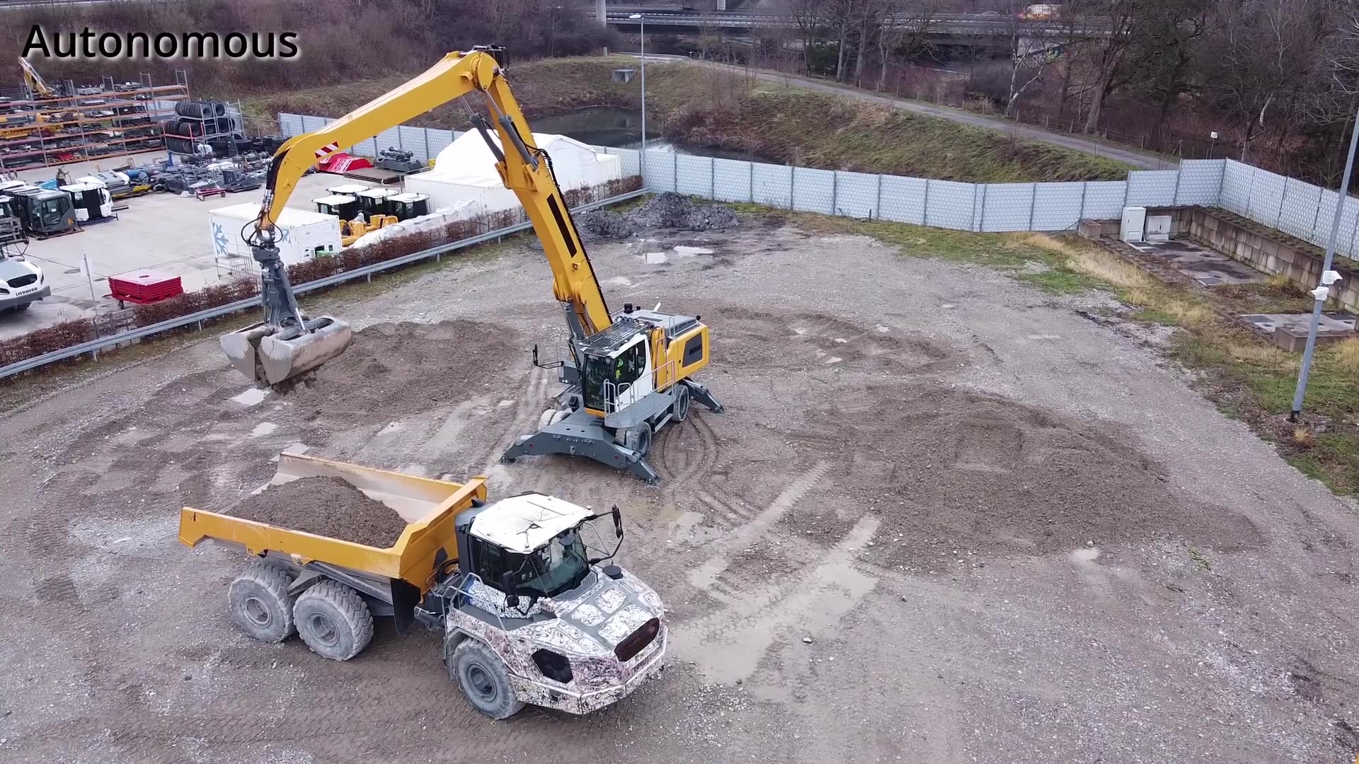 An overhead view of a hydraulic material handler picking up material and unloading it into a truck.